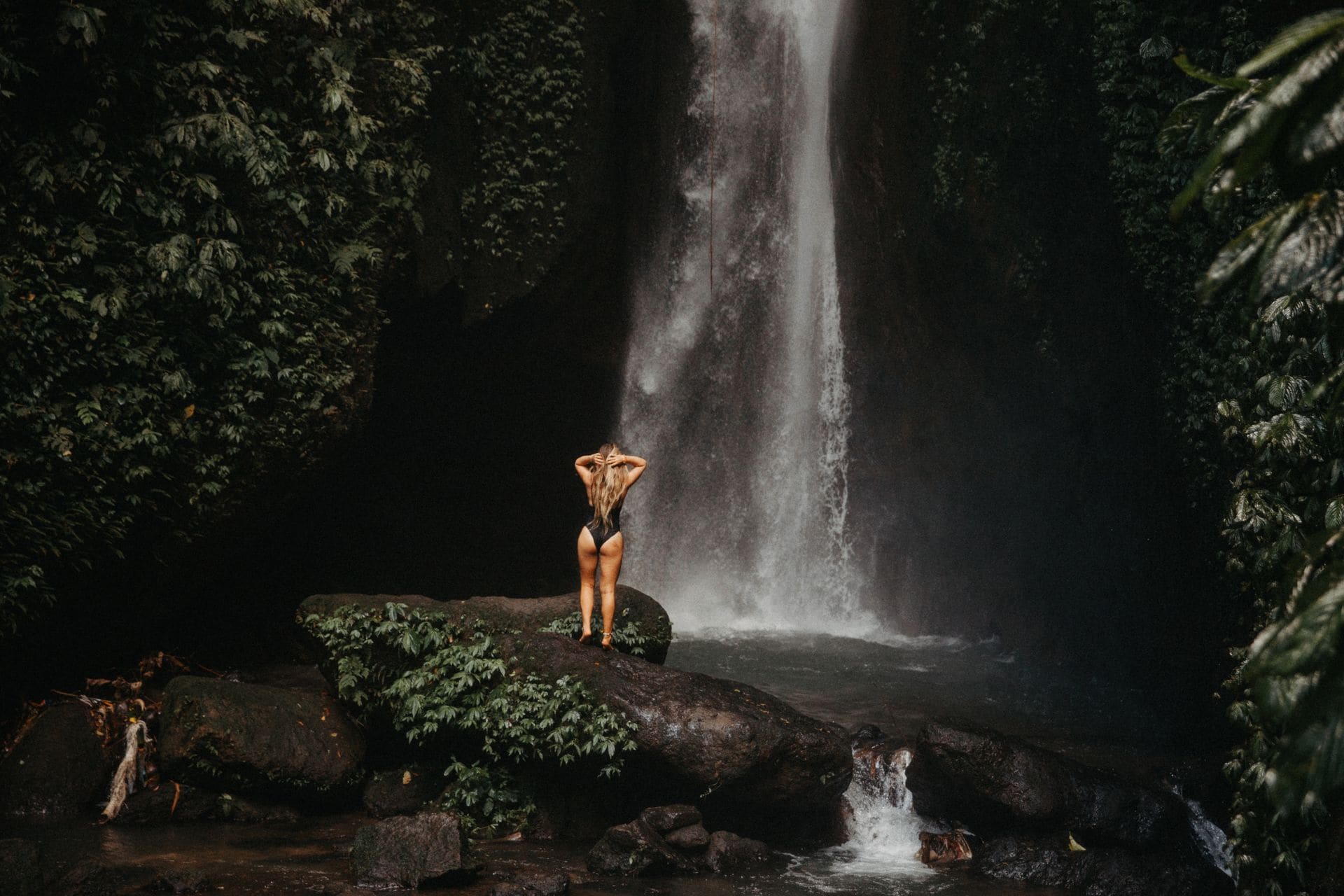 Una mujer se encuentra junto a una serena cascada en la vibrante selva tropical de Bali, abrazando la belleza de la naturaleza.